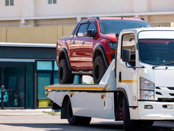 Ein rotes Pickup wird in einer sonnigen städtischen Umgebung auf einen weißen Abschleppwagen von Unfallwagenankauf Gummersbach verladen.